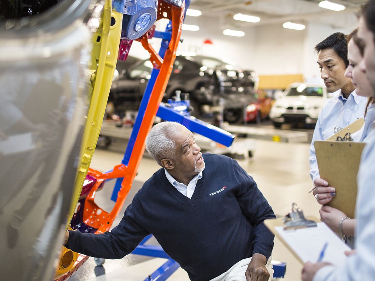 Plant manager kneels by machine equipment while explaining safety measures to inspectors